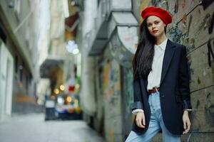 mode vrouw portret wandelen toerist in elegant kleren met rood lippen wandelen naar beneden een versmallen stad straat, reis, filmische kleur, retro wijnoogst stijl, dramatisch tegen een muur met graffitti. foto