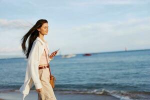 freelance vrouw met telefoon in hand- Aan vakantie wandelen Aan de strand door de oceaan in Bali, gelukkig reizen en vakantie, mobiel communicatie, internet online foto