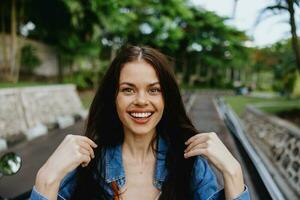 portret van een vrouw brunette glimlach met tanden wandelen buiten tegen een backdrop van palm bomen in de tropen, zomer vakanties en buitenshuis recreatie, de zorgeloos levensstijl van een freelance leerling. foto