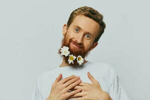 portret van een grappig Mens in een wit t-shirt met bloemen madeliefjes in zijn baard Aan een wit geïsoleerd achtergrond, kopiëren plaats. vakantie concept en Gefeliciteerd. foto