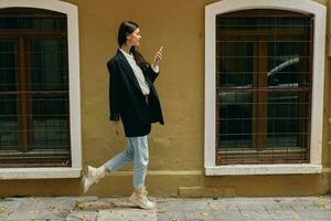 vrouw blogger glimlach met tanden met een telefoon in haar handen wandelingen in de omgeving van de stad mode Aan de straat, voorjaar reis, vakantie in de stad toerist freelancer, mobiel communicatie en internet voor werk foto