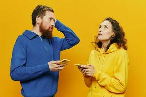 vrouw Mens vrolijk paar met telefoons in hand- sociaal netwerken en communicatie scheef glimlach pret en gevecht, in geel achtergrond. de concept van echt familie verhoudingen, freelancers, werk online. foto