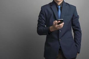 close-up van zakenman in blauw pak met smartphone op grijze achtergrond foto