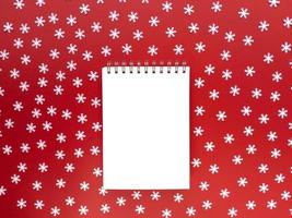 blanco vel notebook met verspreide witte sneeuwvlokken op rode achtergrond. onderwijsconcept. eenvoudig plat leggen met kopieerruimte. Stock foto.