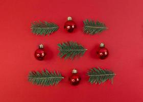 Kerst symmetrie compositie van speelgoed kerstballen en sparren takken op een rode achtergrond. eenvoudig feestelijk plat leggen.
