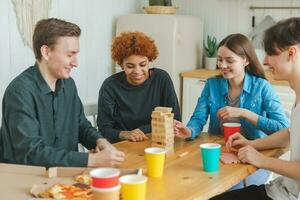 huis feest. vrienden uitgeven tijd samen spelen in bord spel Botsing houten toren Bij huis. gelukkig verschillend groep hebben pret samen binnen. gemengd ras jong maatjes het beste vrienden genieten van weekend. foto