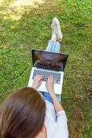 jonge vrouw zittend op groen gras gazon in stadspark werken op laptop pc-computer. freelance bedrijfsconcept foto