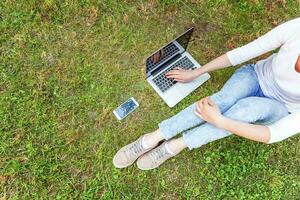 vrouw benen op groen gras gazon in stadspark, handen werken op laptop pc-computer. freelance bedrijfsconcept foto