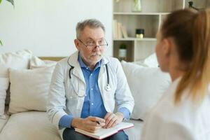 senior Mens dokter onderzoeken yound vrouw in dokter kantoor of Bij huis. meisje geduldig en dokter hebben overleg in ziekenhuis kamer. geneeskunde gezondheidszorg medisch controle. bezoek naar dokter. foto