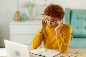 Afrikaanse vrouw aanraken tempels ervaren spanning. meisje Bij huis kantoor moe van werken gevoel hoofdpijn ziek wrijven tempels voorhoofd. lang laptop gebruik computer visie syndroom. kantoor syndroom. foto