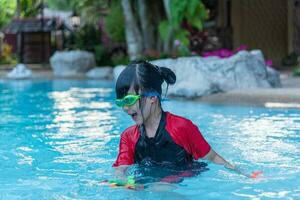 Aziatisch weinig meisje in zwempak spelen met speelgoed Bij zwemmen zwembad gelukkig en hebben plezier. foto