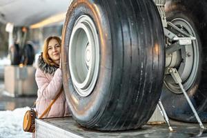 een jonge vrouw kijkt uit van achter grote wielen. het voorste landingsgestel van een passagiersvliegtuig dat op de luchthaven wordt gerepareerd; foto