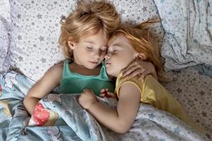 twee kleine zusjes en zusjes die in een omhelzing in bed slapen onder één deken foto