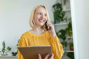 attent vrouw Holding papier terwijl pratend Aan mobiel telefoon. vrouw is op zoek door venster. ze is Bij huis. foto