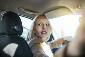 vrouw in auto binnen- draaien in de omgeving van op zoek Bij passagiers in terug stoel idee taxi bestuurder. concept van tentamen voertuig. terug visie van een aantrekkelijk jong vrouw op zoek over- haar schouder terwijl het rijden een auto. foto