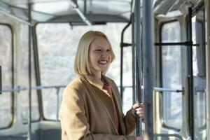 een jong vrouw glimlachen in een bus terwijl op zoek door de venster mooi jong vrouw nemen bus naar werk. passagier in de bus of trein, technologie levensstijl, vervoer en op reis concept. foto