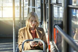 modern glimlachen schattig vrouw zittend in een bus . glimlachen en op zoek weg. bus reis. vrouw gebruik makend van haar cel telefoon Aan bus. tram. sms, bericht. vrouw met telefoon Bij de openbaar vervoer foto