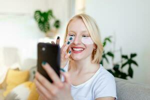 mooi jong glimlachen brunette vrouw met schoonheidsmiddelen masker, oog patches en gebruik makend van een telefoon. aantrekkelijk vrouw is berichten Aan telefoon foto