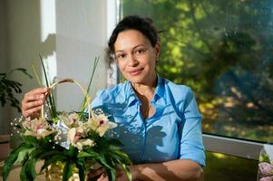 charmant vrouw bloemist, bedrijf baasje, glimlachen Bij camera, Holding mooi boeket van bloemen in rieten mand foto