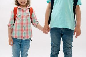 detailopname tiener jongen en kleuter meisje Holding handen, geïsoleerd Aan wit achtergrond. kinderen met rugzak gaan naar de school- foto