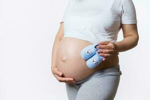 detailopname gravid vrouw strelen haar buik, Holding schattig baby slofjes bovenstaand haar groot zwanger buik, in de laat zwangerschap foto