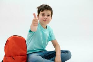 detailopname studio portret van een slim tiener- school- jongen, duimen omhoog, op zoek Bij camera, geïsoleerd wit achtergrond foto