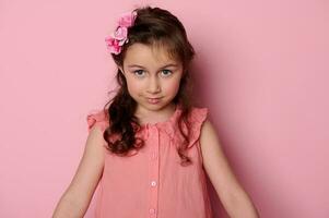 Kaukasisch weinig meisje 6 jaren oud, met blauw ogen en elegant kapsel, gekleed in elegant roze jurk op zoek Bij camera foto