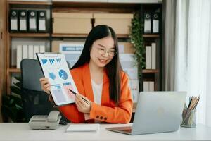 zelfverzekerd Aziatisch vrouw met een glimlach staand Holding kladblok en tablet Bij de kantoor. foto