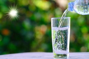 hand gietend water in een glazen beker met een bokeh-aardachtergrond foto