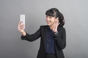 mooie zakenvrouw die smartphone op grijze achtergrond gebruikt foto