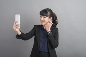mooie zakenvrouw die smartphone op grijze achtergrond gebruikt foto