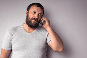 bebaarde man in grijs t-shirt met mobiele telefoon foto
