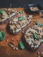 smakelijke verse bruschetta met champignons, spinazie, knoflook, roomkaas en pijnboompitten, op een houten bord, op een donkere achtergrond. foto