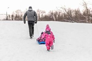 papa en zijn twee kinderen spelen en gaan sleeën in het park. foto