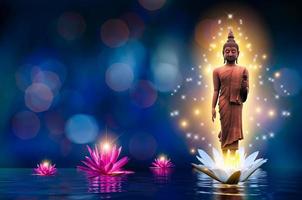 het boeddhabeeld staat op een witte en roze lotus in het water. bokeh blauwe achtergrond. foto