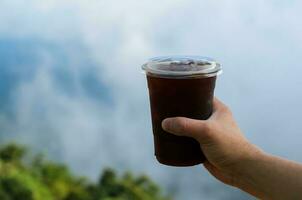 hand- Holding een glas van bevroren koffie met wazig berg en wolk achtergrond. zomer drinken concept. foto