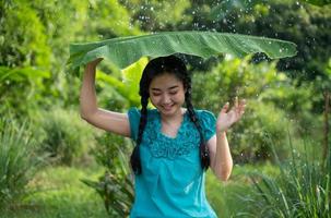 portret van een jonge Aziatische vrouw met zwart haar met een bananenblad in het regent op de groene tuin achtergrond foto