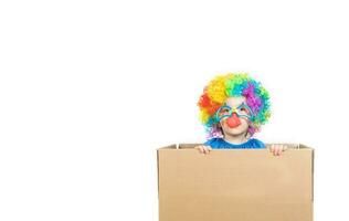 jongen van vijf jaren gekleed in de kostuum van een clown blijft in een karton papier doos. foto