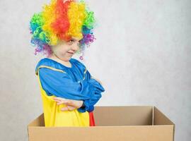jongen van vijf jaren gekleed in de kostuum van een clown blijft in een karton papier doos. foto