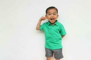 portret van een schattig weinig Aziatisch jongen Holding zijn oor terwijl plakken zijn tong uit, geïsoleerd Aan de wit achtergrond foto