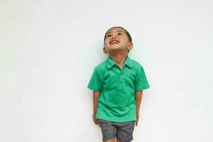 portret van een gelukkig weinig Aziatisch jongen nieuwsgierig op zoek omhoog terwijl lachend, geïsoleerd Aan de wit achtergrond foto