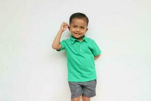 portret van een schattig weinig Aziatisch jongen glimlachen terwijl Holding zijn oor op zoek Bij camera, geïsoleerd Aan de wit achtergrond foto