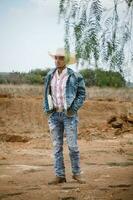 cowboy vervelend jeans en een hoed, staand onder de lucht met pluizig wolken, werken Aan een boerderij foto