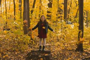 weinig meisje kind het werpen herfst bladeren Aan natuur achtergrond - vallen seizoen en kinderen vrije tijd concept foto