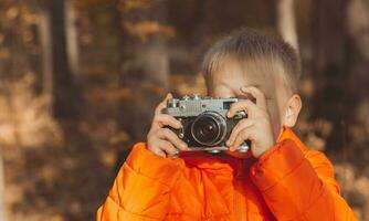 jongen met retro camera nemen afbeeldingen buitenshuis in herfst natuur. vrije tijd en fotografen concept foto