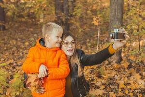 zoon en moeder zijn nemen selfie Aan camera in herfst park. single ouder, vrije tijd en vallen seizoen concept. foto