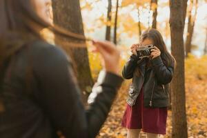 kind nemen afbeelding haar moeder Aan retro camera in herfst park. hobby's en vrije tijd concept. foto