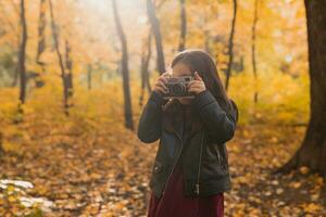 kind meisje gebruik makend van een oubollig camera in herfst natuur. fotograaf, vallen seizoen en vrije tijd concept. foto