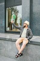 gebaard Mens duurt selfie via smartphone wandelingen in downtown poses tegen modern stad gebouw geniet vrije tijd tijd. mensen stedelijk levensstijl en technologie concept foto
