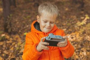 jongen met retro camera nemen afbeeldingen buitenshuis in herfst natuur. vrije tijd en fotografen concept foto